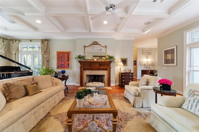 living room with coffered ceiling, a tile fireplace, ornamental molding, and light wood-type flooring