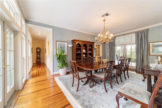 dining area with an inviting chandelier, crown molding, light wood-type flooring, and french doors