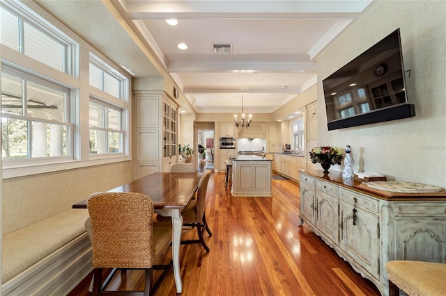 dining room with beamed ceiling, a notable chandelier, ornamental molding, and light wood-type flooring