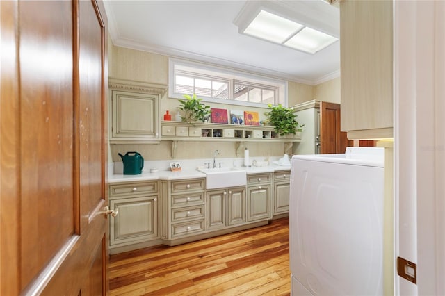 clothes washing area with washer / dryer, cabinets, light hardwood / wood-style flooring, ornamental molding, and sink