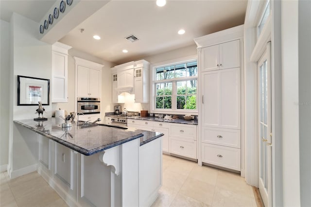 kitchen featuring oven, a kitchen bar, kitchen peninsula, white cabinets, and dark stone countertops