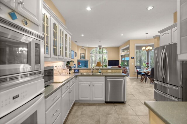 kitchen with light tile patterned floors, a peninsula, a sink, appliances with stainless steel finishes, and a notable chandelier