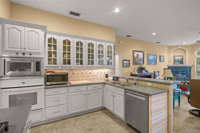 kitchen featuring visible vents, a peninsula, a sink, stainless steel appliances, and a glass covered fireplace