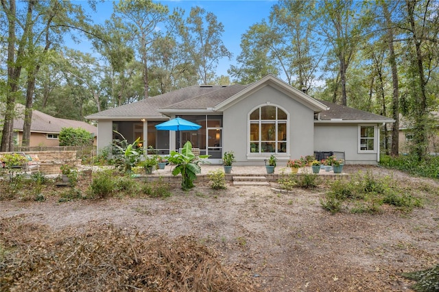 rear view of house with stucco siding, a patio area, a shingled roof, and a sunroom