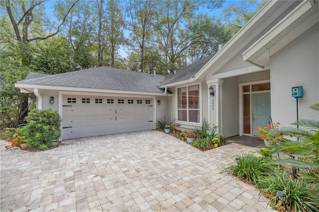 exterior space featuring roof with shingles, decorative driveway, an attached garage, and stucco siding