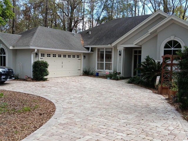 single story home featuring roof with shingles, stucco siding, an attached garage, and curved driveway