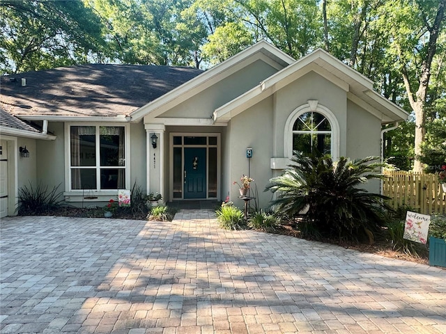 view of exterior entry featuring stucco siding, fence, and roof with shingles