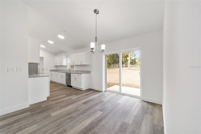 kitchen with lofted ceiling, white cabinets, hanging light fixtures, stainless steel dishwasher, and wood-type flooring