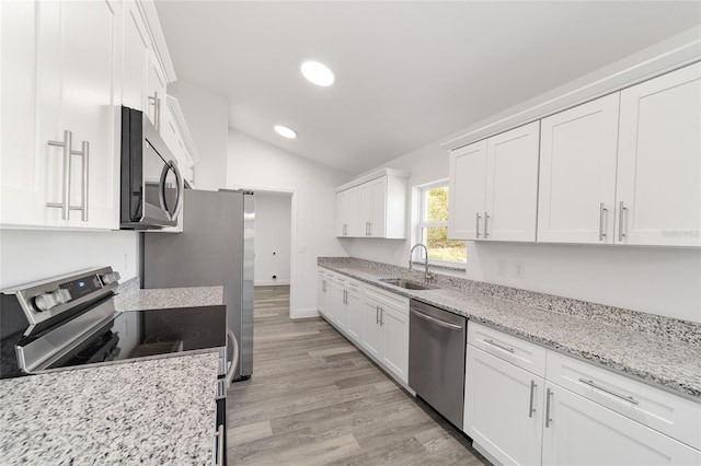 kitchen with sink, appliances with stainless steel finishes, vaulted ceiling, and white cabinets