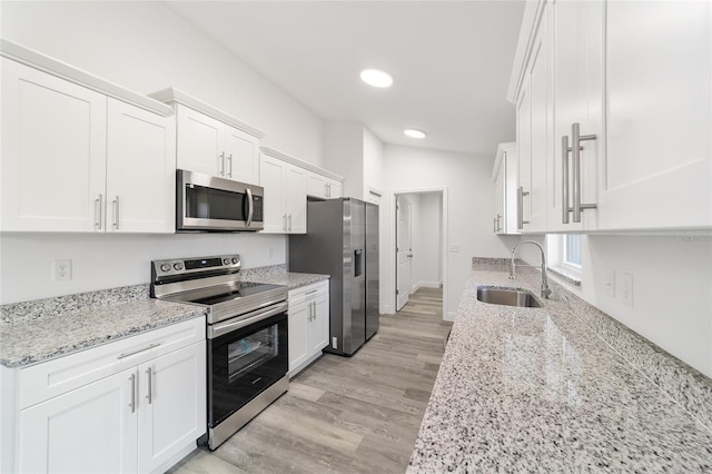 kitchen with white cabinets, appliances with stainless steel finishes, light stone countertops, light wood-type flooring, and sink