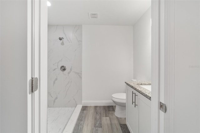 bathroom featuring vanity, hardwood / wood-style floors, toilet, and a tile shower