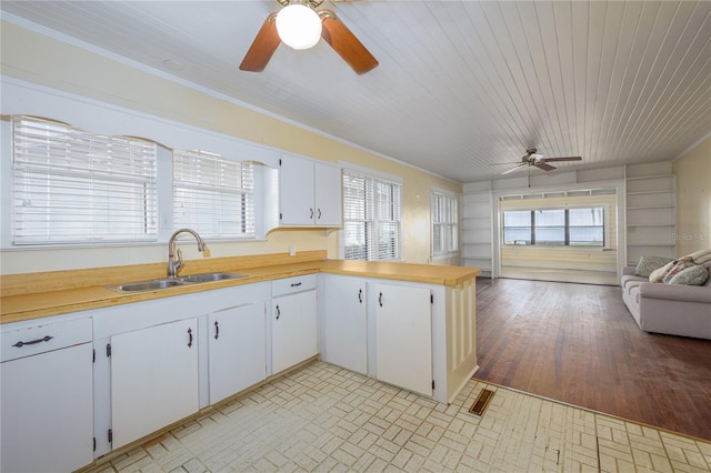 kitchen featuring kitchen peninsula, white cabinetry, light hardwood / wood-style flooring, ornamental molding, and sink