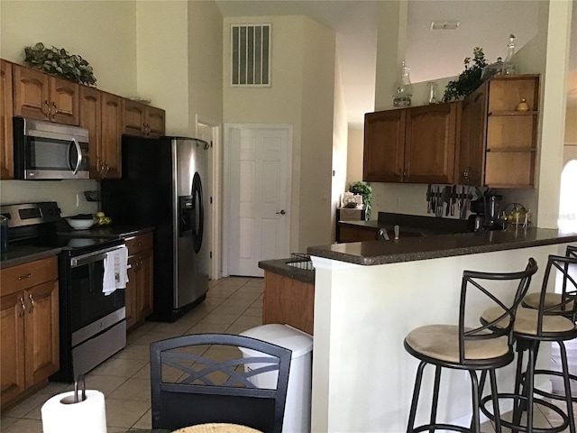 kitchen with light tile patterned floors, stainless steel appliances, a breakfast bar area, and kitchen peninsula