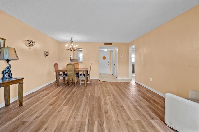 dining space with an inviting chandelier, a textured ceiling, and light wood-type flooring