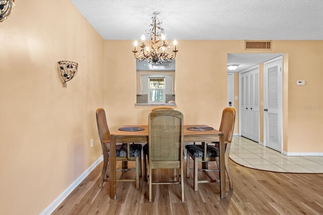 dining area featuring light hardwood / wood-style floors, a notable chandelier, and a textured ceiling