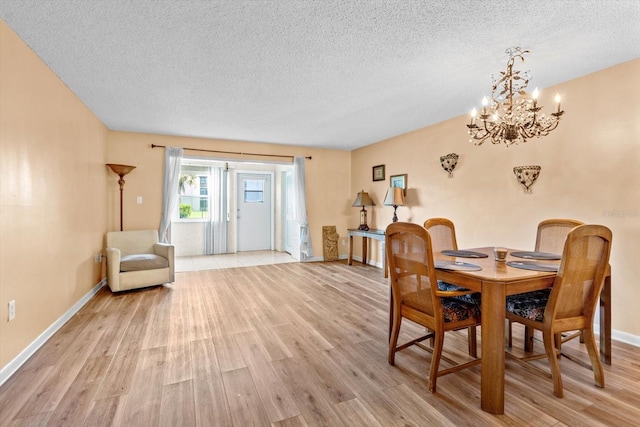 dining area with light hardwood / wood-style flooring, a textured ceiling, and an inviting chandelier