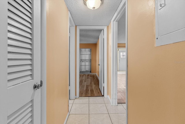 hallway featuring a textured ceiling, electric panel, and light tile patterned floors