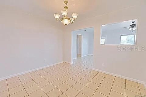 spare room with light tile patterned flooring and ceiling fan with notable chandelier