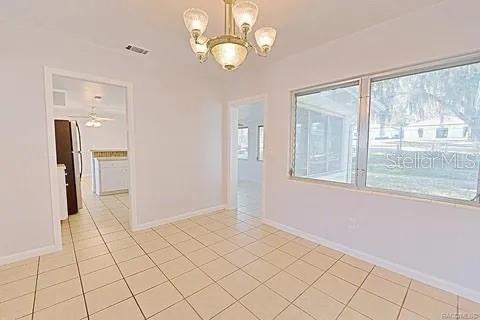 tiled spare room featuring ceiling fan with notable chandelier