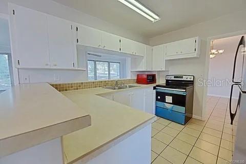 kitchen featuring stainless steel appliances, sink, light tile patterned flooring, an inviting chandelier, and white cabinets