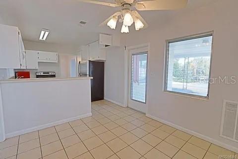 kitchen featuring black refrigerator, stainless steel range with electric stovetop, light tile patterned floors, white cabinets, and ceiling fan