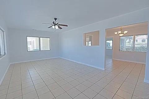 tiled spare room featuring ceiling fan with notable chandelier