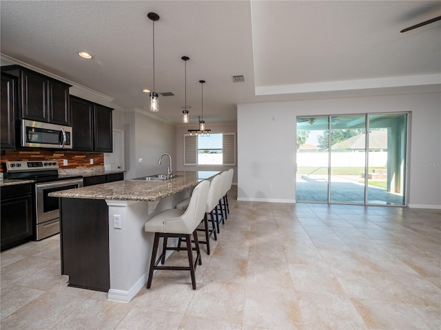 kitchen featuring sink, backsplash, a kitchen breakfast bar, stainless steel appliances, and a center island with sink