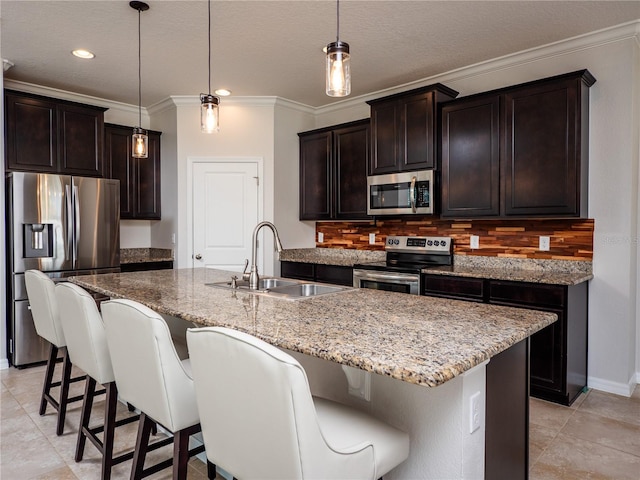 kitchen with tasteful backsplash, hanging light fixtures, an island with sink, sink, and stainless steel appliances