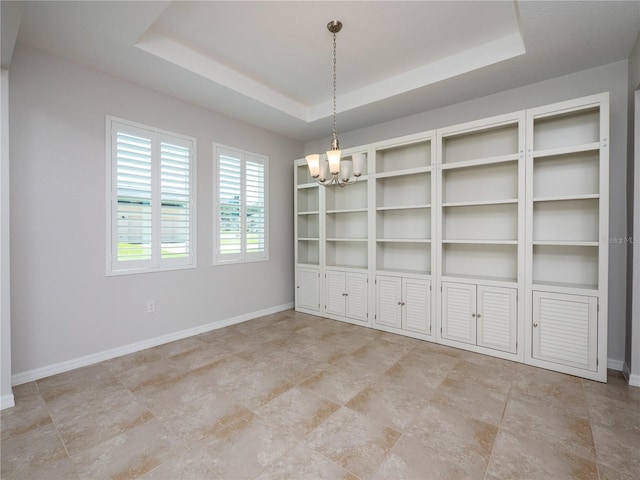 unfurnished dining area featuring a raised ceiling and a chandelier