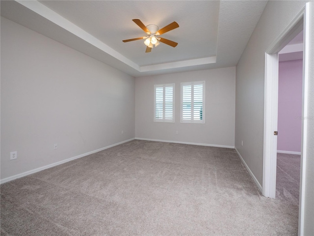 spare room featuring a raised ceiling, light carpet, and ceiling fan