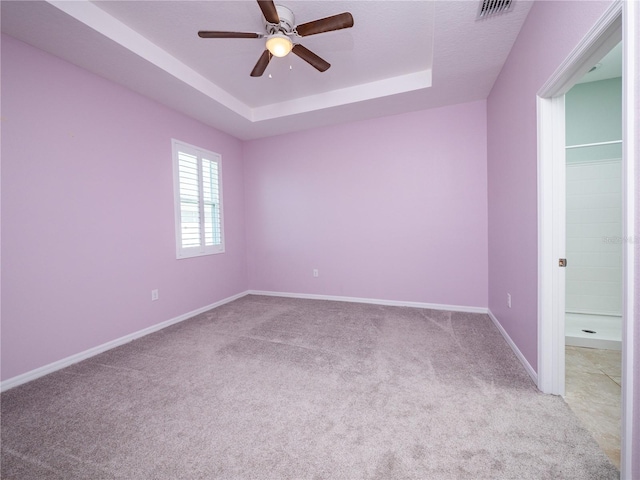 empty room with ceiling fan, light carpet, and a raised ceiling