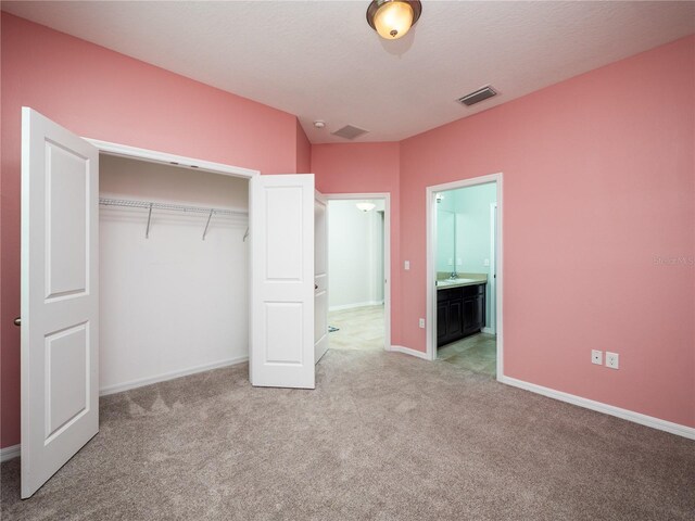 unfurnished bedroom with a closet, a textured ceiling, ensuite bathroom, and light colored carpet