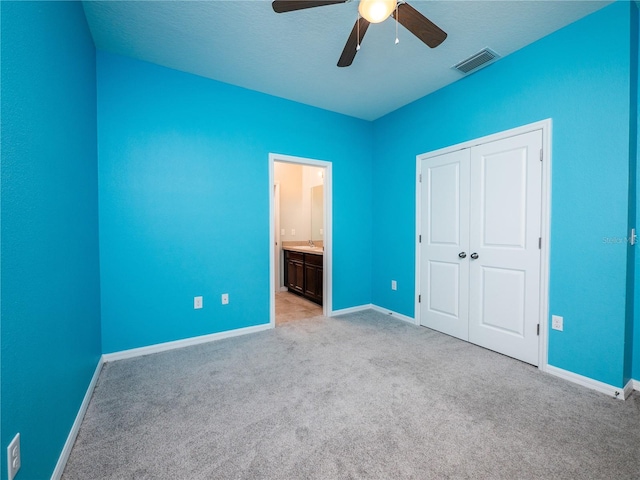 unfurnished bedroom featuring ensuite bathroom, a textured ceiling, a closet, ceiling fan, and light carpet