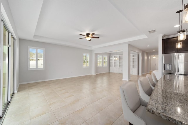 tiled living room featuring built in shelves, ceiling fan, and a tray ceiling