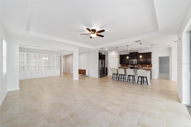 living room with built in shelves, a tray ceiling, and ceiling fan with notable chandelier