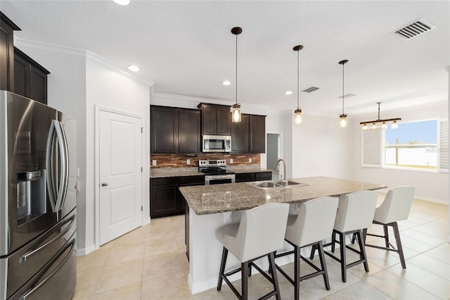 kitchen with hanging light fixtures, a center island with sink, sink, and appliances with stainless steel finishes