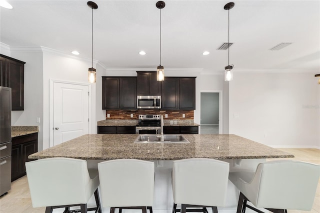 kitchen with pendant lighting, stainless steel appliances, and a center island with sink