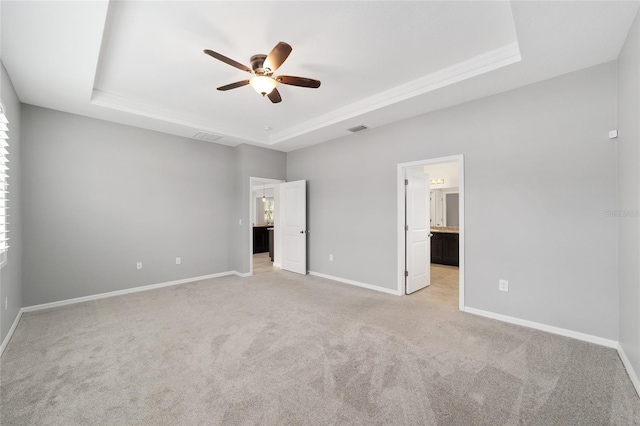 unfurnished bedroom with light carpet, connected bathroom, a tray ceiling, and ceiling fan