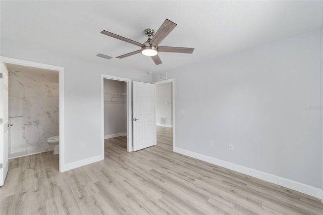 unfurnished bedroom with connected bathroom, ceiling fan, light wood-type flooring, and a walk in closet