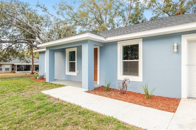 entrance to property featuring a yard, roof with shingles, covered porch, and stucco siding