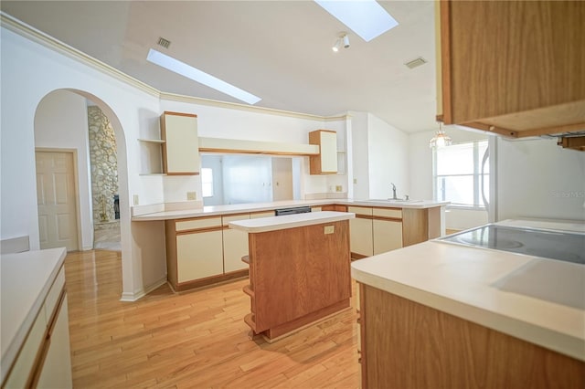 kitchen featuring kitchen peninsula, a center island, light wood-type flooring, ornamental molding, and sink