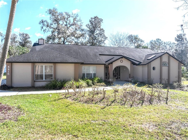 view of front of home featuring a shingled roof, a chimney, a front lawn, and stucco siding