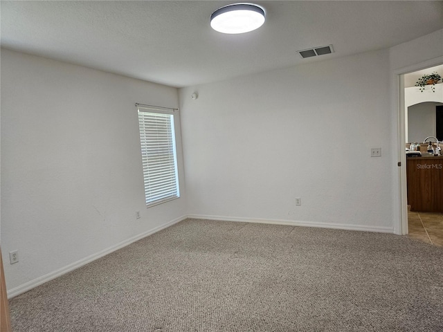spare room with baseboards, light carpet, and visible vents