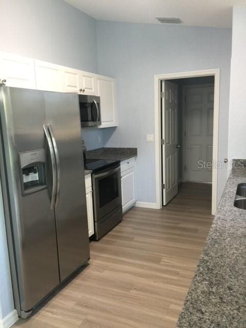 kitchen featuring white cabinets, light hardwood / wood-style flooring, stainless steel appliances, and dark stone countertops