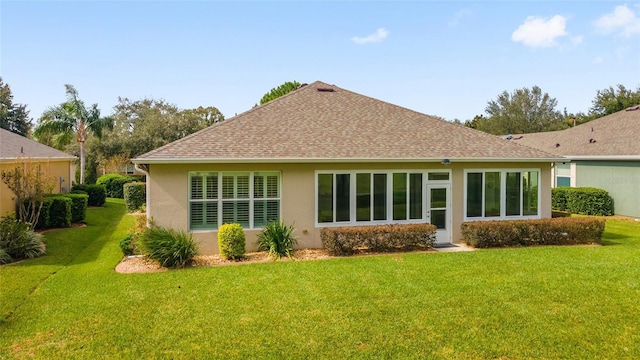 rear view of house featuring roof with shingles, stucco siding, and a lawn