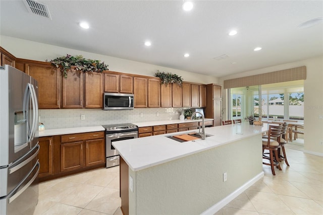 kitchen with backsplash, a center island with sink, sink, light tile patterned floors, and appliances with stainless steel finishes