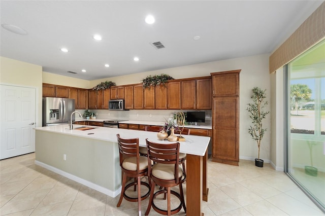 kitchen with appliances with stainless steel finishes, sink, light tile patterned floors, a breakfast bar area, and an island with sink