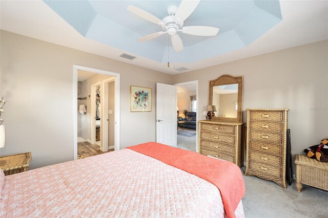 carpeted bedroom with ensuite bathroom, ceiling fan, and a tray ceiling