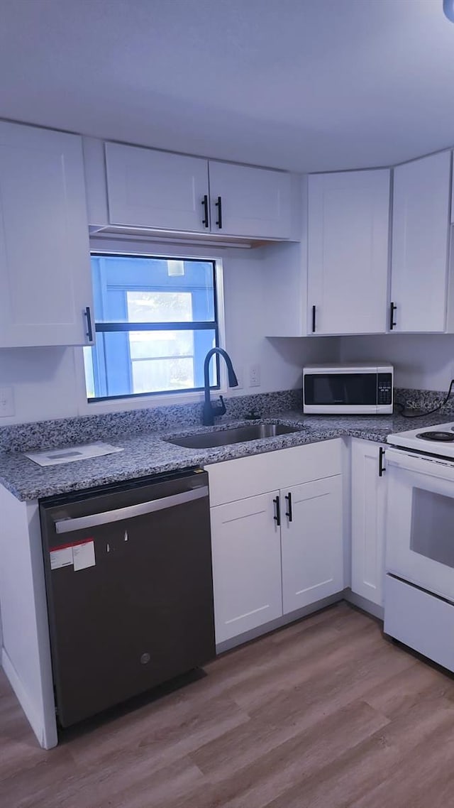 kitchen featuring white appliances, sink, dark stone counters, white cabinets, and light hardwood / wood-style flooring