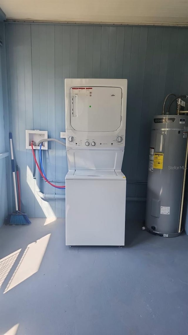 clothes washing area with wood walls, electric water heater, and stacked washer and clothes dryer